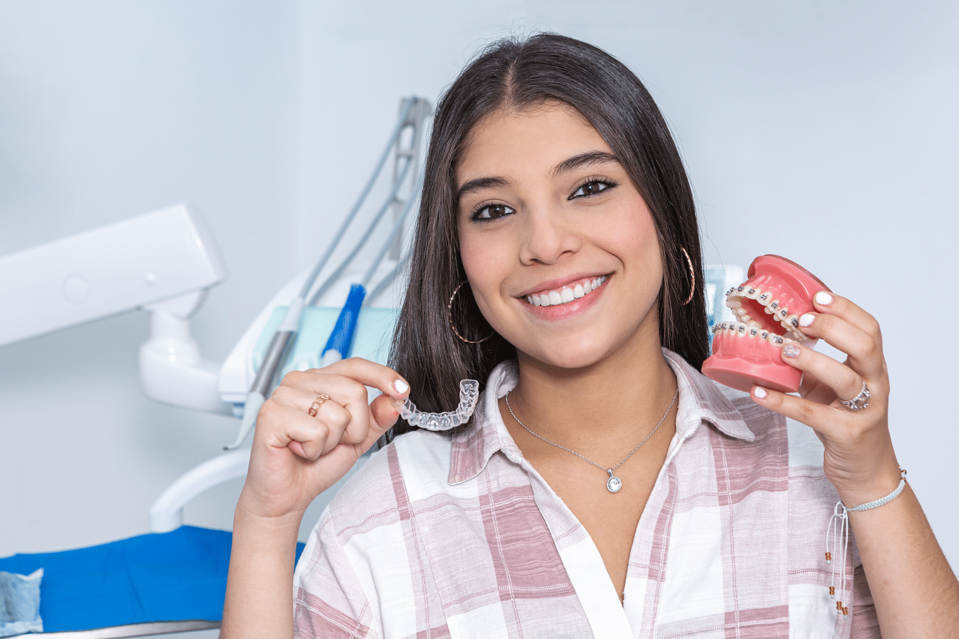 Smiling teen holding a clear aligner and a dental model with braces