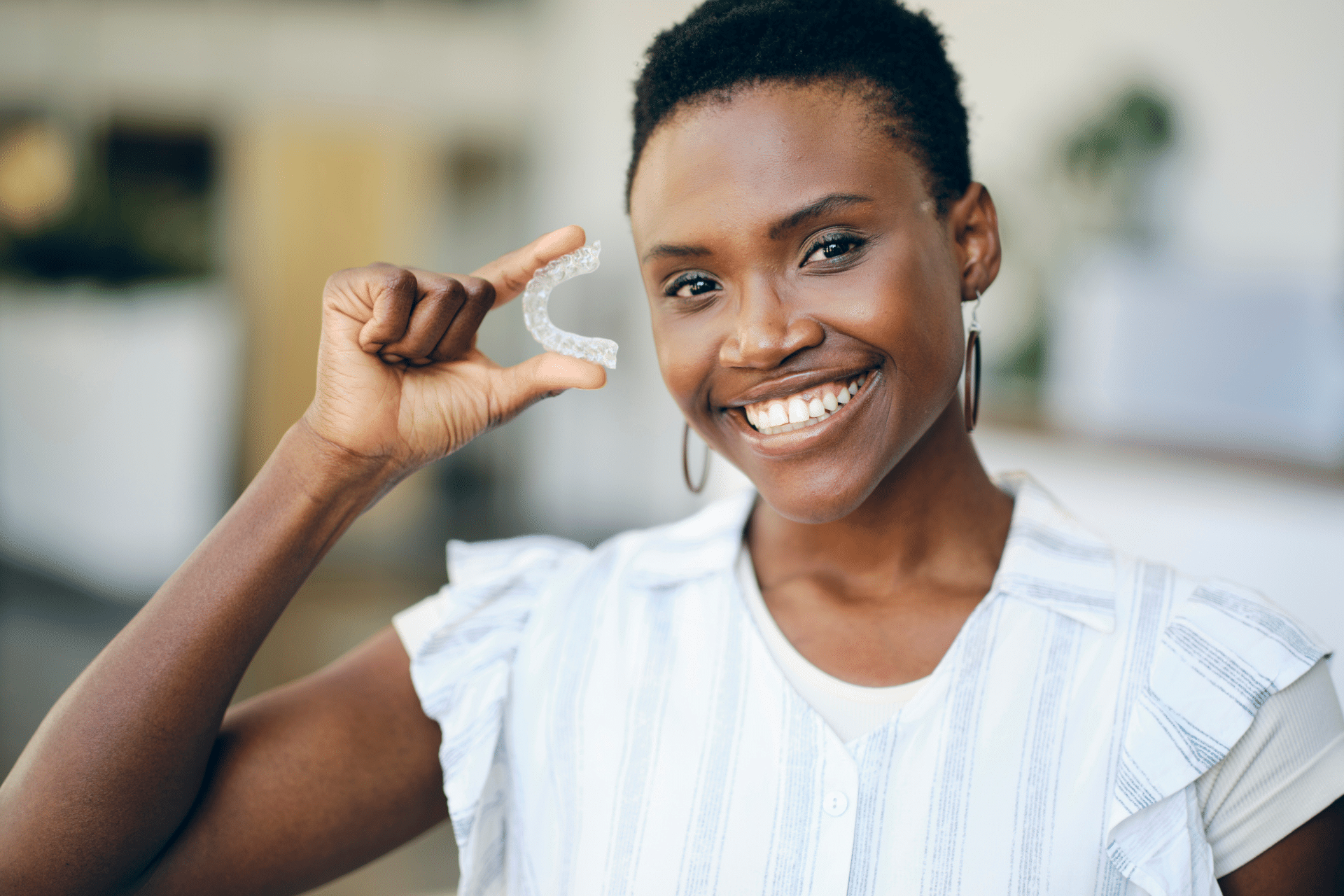 Smiling woman with short hair holding up a clear aligner tray next to her cheek